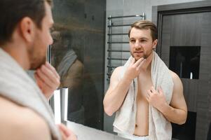 Young man looking in mirror after shaving at home photo