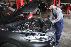 sonriente mecánico utilizando un ordenador portátil ordenador personal a el reparar cochera. foto