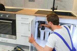 Repairman In Overalls Repairing Cabinet Hinge In Kitchen photo