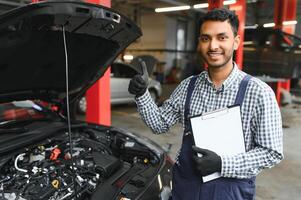Indian car mechanic standing and working in service station. Car specialists examining the lifted car. Professional repairmen wearing mechanic uniform in blue color. photo