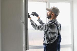 Workman in overalls installing or adjusting plastic windows in the living room at home photo