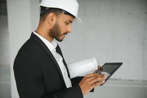 confidente asiático ingeniero hombre utilizando tableta para comprobación y mantenimiento a inspección a moderno hogar edificio construcción. arquitecto trabajando con blanco la seguridad casco en construcción sitio. foto