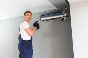 hermoso joven hombre electricista instalando aire acondicionamiento en un cliente casa foto