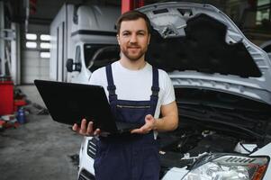 auto servicio, reparar, mantenimiento concepto. mecánico cheques el auto, haciendo diagnósticos con ordenador portátil a el Servicio estación. Servicio mantenimiento de industrial a motor reparar. foto