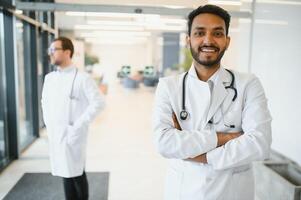 Portrait of male indian doctor wearing white coat having open door on clinic corridor as background photo