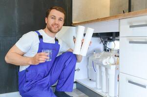 Plumber installs or change water filter. Replacement aqua filter. Repairman installing water filter cartridges in a kitchen. Installation of reverse osmosis water purification system. photo