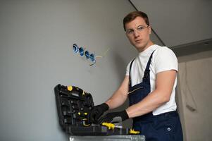 Electrician in uniform mounting electric sockets on the white wall indoors photo