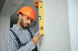 Indian male construction worker standing in uniform and hard hat at construction site. photo