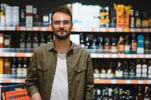 un hombre toma alcohólico bebidas desde el supermercado estante. compras para alcohol en el Tienda foto