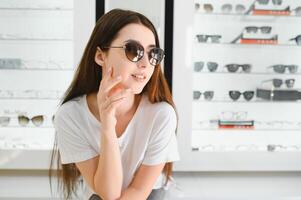 Happy Woman Wearing Sunglasses in a Optical Store. Cheerful girl trying trendy shades on sale photo