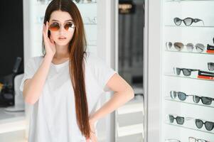 un joven mujer elige en Gafas de sol en un óptica Tienda foto