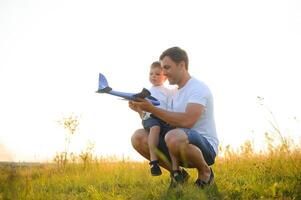 linda pequeño chico y su hermoso joven papá son sonriente mientras jugando con un juguete avión en el parque. foto