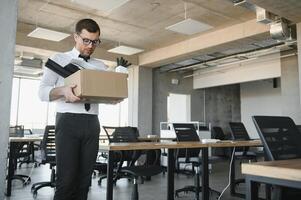 Sad Fired. Let Go Office Worker Packs His Belongings into Cardboard Box and Leaves Office. Workforce Reduction, Downsizing, Reorganization, Restructuring, Outsourcing. Mass Unemployment Market Crisis photo