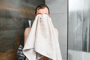 alegre joven hombre limpiando cara con suave toalla después Lavado eso en el Mañana foto