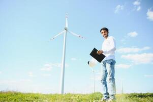 ingeniero India hombre trabajando a molino granja generando electricidad limpiar energía. viento turbina granja generador por alternativa verde energía. asiático ingeniero comprobación controlar eléctrico poder foto