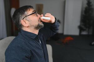 retrato de hombre con un nasal rociar. enfermo hombre utilizando nariz gotas mientras tendido a el cama. concepto de tratamiento para alergias o el común frío, invierno estilo. foto