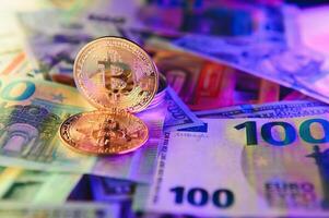 Close up heap of golden bitcoin physical coins on top of Euro, dollar banknotes background, high angle view, selective focus photo