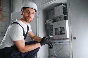 hombre, un eléctrico técnico trabajando en un tablero de conmutadores con fusibles. instalación y conexión de eléctrico equipo. profesional con herramientas en mano. concepto de complejo trabajar, espacio para texto. foto