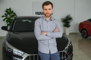 Final decision. Shot of a handsome young man standing in front of a new car at the dealership thinking rubbing his chin photo