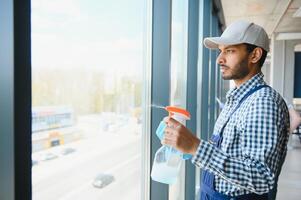 Young indian man washing window in office. photo