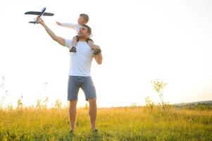 contento padre niño momento. padre llevar a cuestas su chico a puesta de sol mientras él es jugando con juguete avión. foto