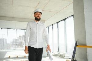 Portrait of good-looking Middle Eastern guy wearing safety helmet and holding construction plan. Employees and business concept. photo