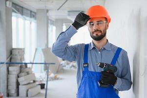 Portrait of young and hardworking constructor posing in big unfinished room. Building concept photo