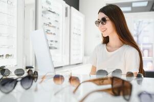 Happy Woman Wearing Sunglasses in a Optical Store. Cheerful girl trying trendy shades on sale photo