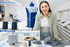 Young dressmaker woman sews clothes on working table. Smiling seamstress and her hand close up in workshop. photo