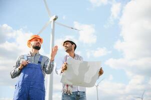 indian and european male engineers working on wind farm with windmills. photo