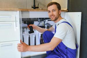 Repairman In Overalls Repairing Cabinet Hinge In Kitchen photo