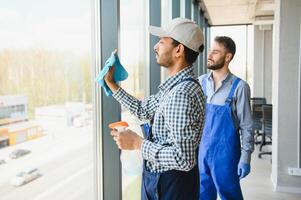 multiétnico profesional limpiadores en uniforme Lavado grande ventanas en oficina foto