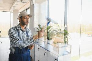 joven indio hombre Lavado ventana en oficina foto