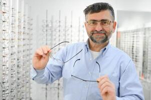 lentes controlar, mayor visión y mayor hombre a un consultante optometría clínica para bienestar. feliz, sonrisa y antiguo cara con lente, marco y gafas elección en un Tienda para ayuda consiguiendo un prescripción. foto