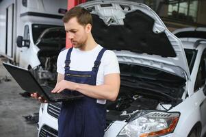 auto servicio, reparar, mantenimiento concepto. mecánico cheques el auto, haciendo diagnósticos con ordenador portátil a el Servicio estación. Servicio mantenimiento de industrial a motor reparar. foto