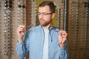 Young man choosing spectacles at optic shop photo