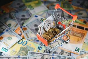 Close up heap of golden bitcoin physical coins on top of Euro, dollar banknotes background, high angle view, selective focus photo