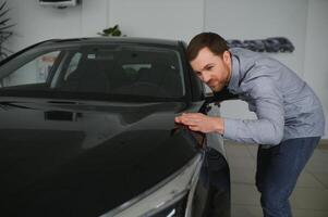 Visiting car dealership. Handsome bearded man is stroking his new car and smiling photo