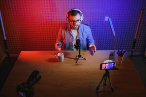 Young man recording or streaming podcast using microphone at his small broadcast studio. Content creator. photo