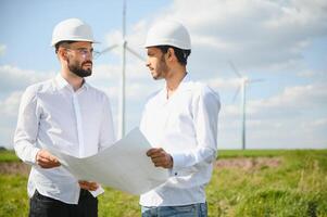 indian and european male engineers working on wind farm with windmills. photo