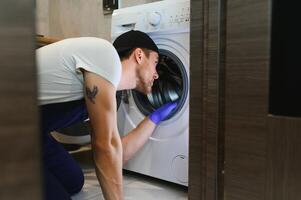 el joven hermoso reparador en trabajador traje con el profesional herramientas caja es fijación el Lavado máquina en el baño foto