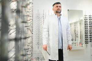 Portrait of a handsome ophthalmologist in front of the showcase with eyeglasses in the hospital. photo