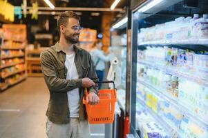 Portrait of smiling handsome man grocery shopping in supermarket, choosing food products from shelf photo