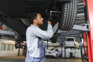 latín Hispano auto mecánico en uniforme es examinando un coche mientras trabajando en auto Servicio foto