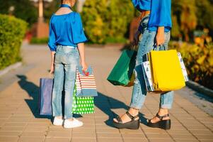 venta, consumismo y personas concepto - contento joven mujer su hija con compras pantalones caminando ciudad calle foto