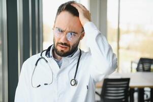 Stressed male doctor. Mid adult male doctor working long hours. Overworked doctor in his office. Not even doctors are exempt from burnout photo