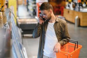 Handsome young man check the fridges for frozen food in the supermarket. photo