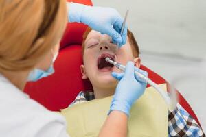 pediátrico dentista examinando un pequeño Niños dientes en el dentistas silla a el dental clínica foto