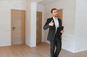 A successful real estate agent stands in a new modular building and offers a new home photo