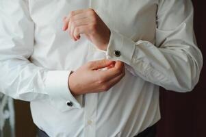 A businessman dresses a white shirt close-up, the groom prepares for the wedding ceremony. Male style. Shirts and collar cuffs photo